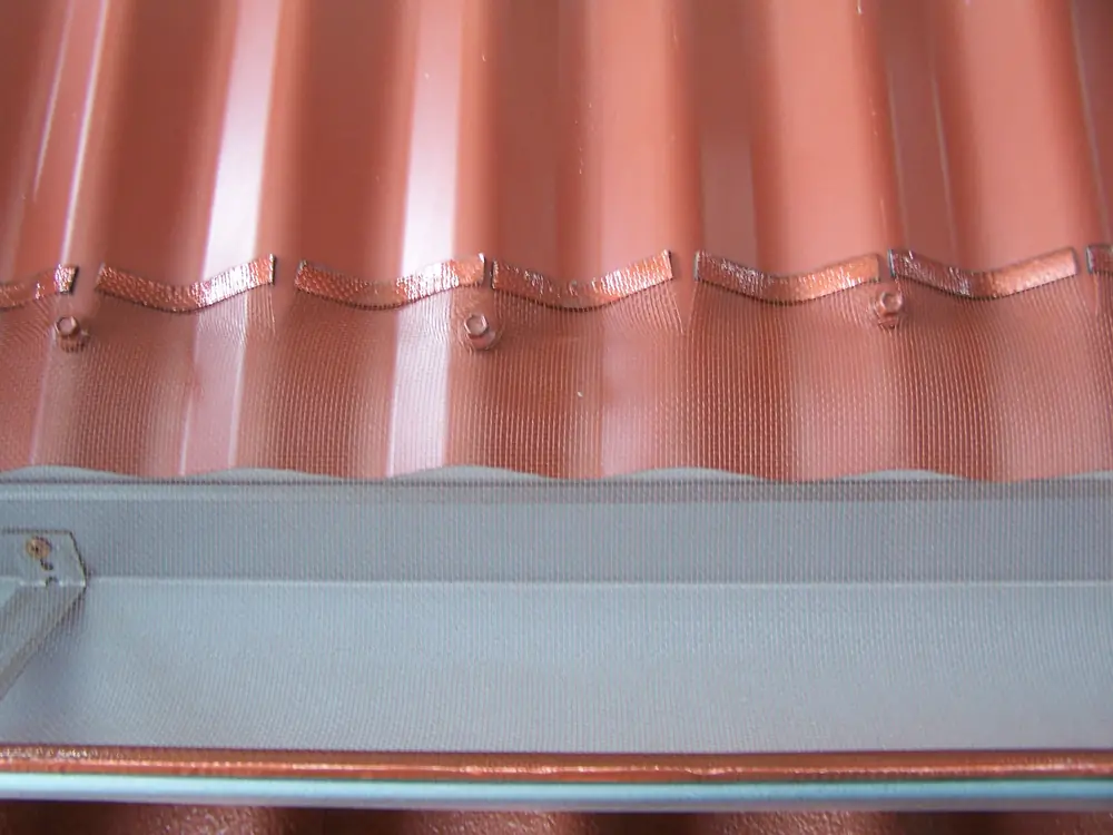 Close detail of saddles holding gutter mesh at the edge of a terracotta tiled roof