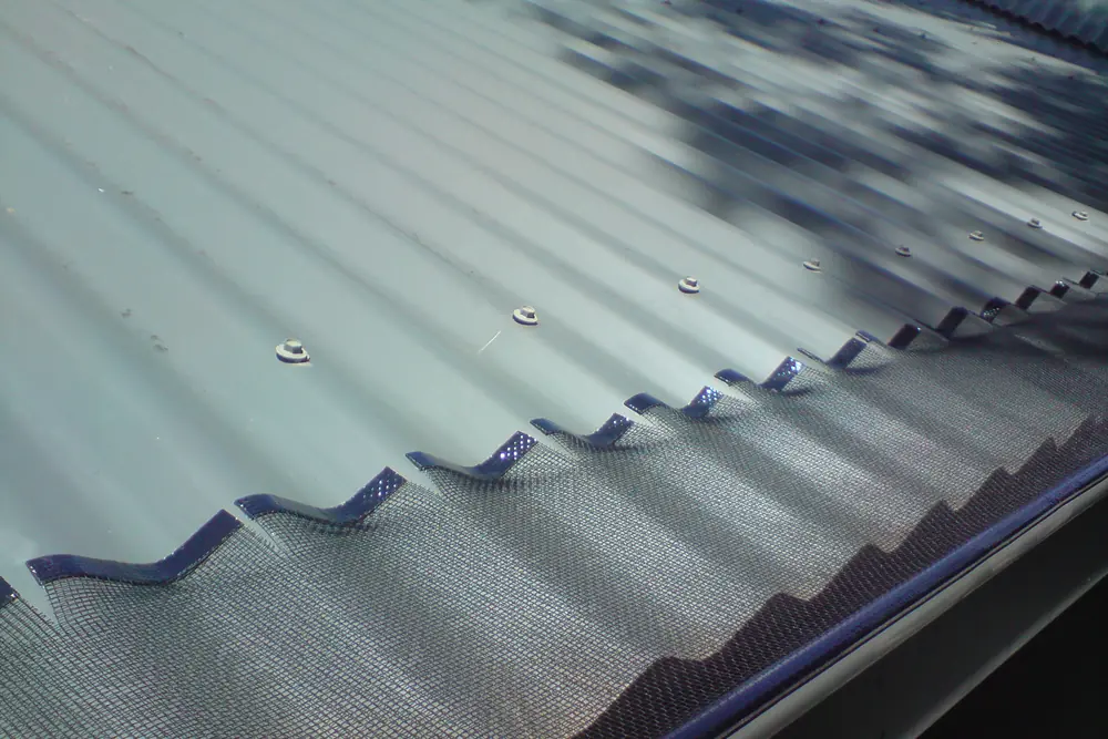 Close view of gutter mesh laid over the corrugations of a metal roof