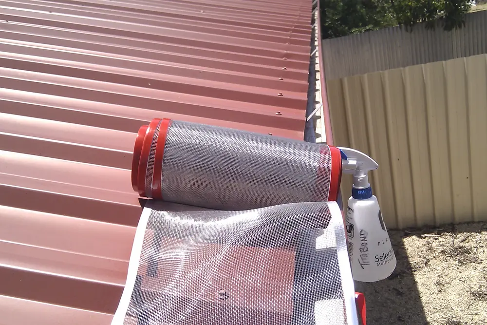 A roll of gutter mesh and a spray bottle of surface cleaner on a roof before fitting